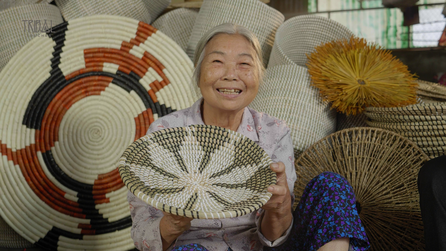 Grandma Lan smiling while proudly holding her handcrafted seagrass basket at Tribal Touches.
